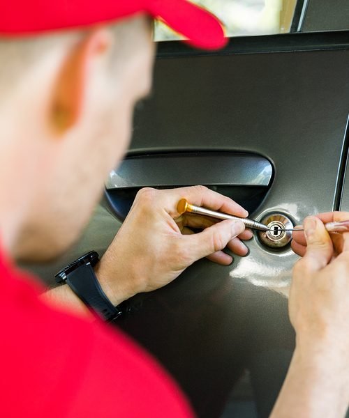 locksmith in red uniform opening car door with lockpicker